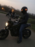 Motorrijder zit op zijn stilstaande motor bij een stopplaats, op zijn helm de LED-vizierstrip met oranje pixelogen en het LED-achterpaneel met een pixelhart